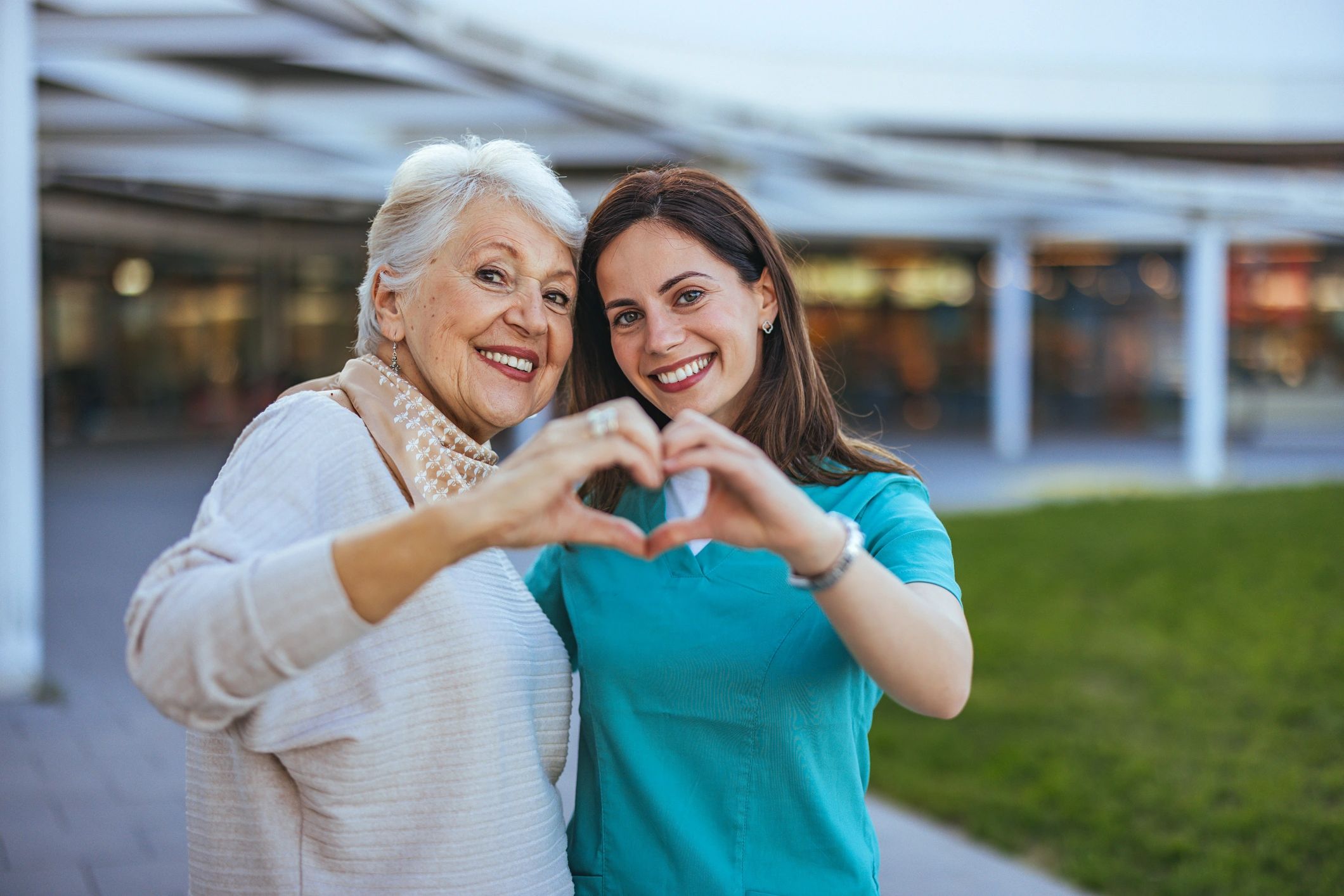 Two women making a heart shape with their hands outdoors